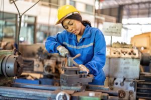 Woman worker in uniform operating machine at factory concentrate on fabrication job on lathe