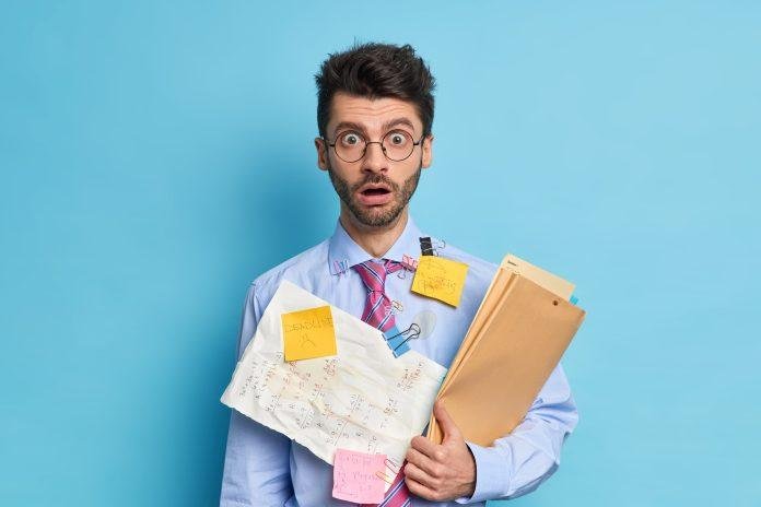 Shocked male student has papers with written math solution greatly surprised to have deadline wears